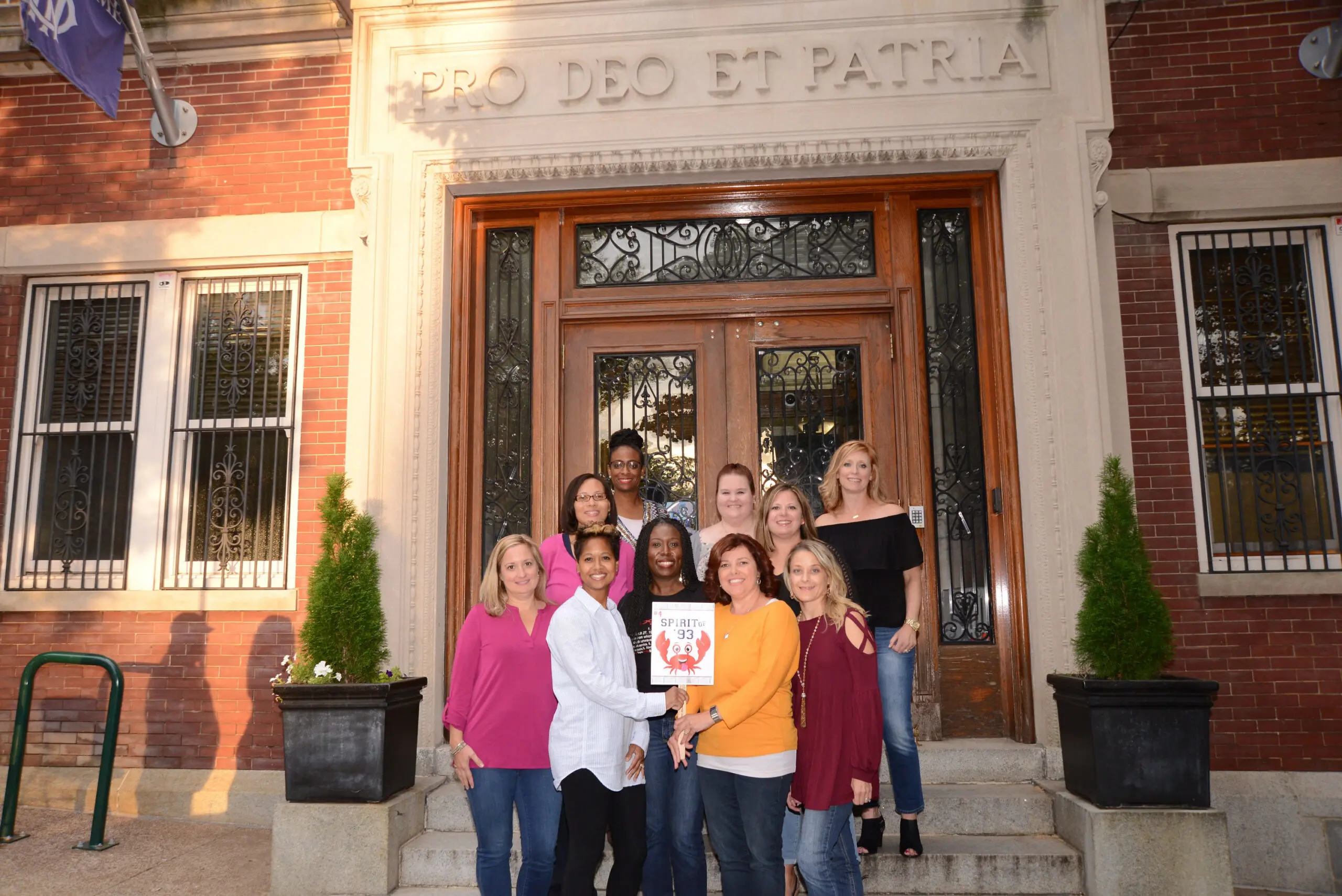 A group of women gathered in front of a house holding a sign with a crab on it