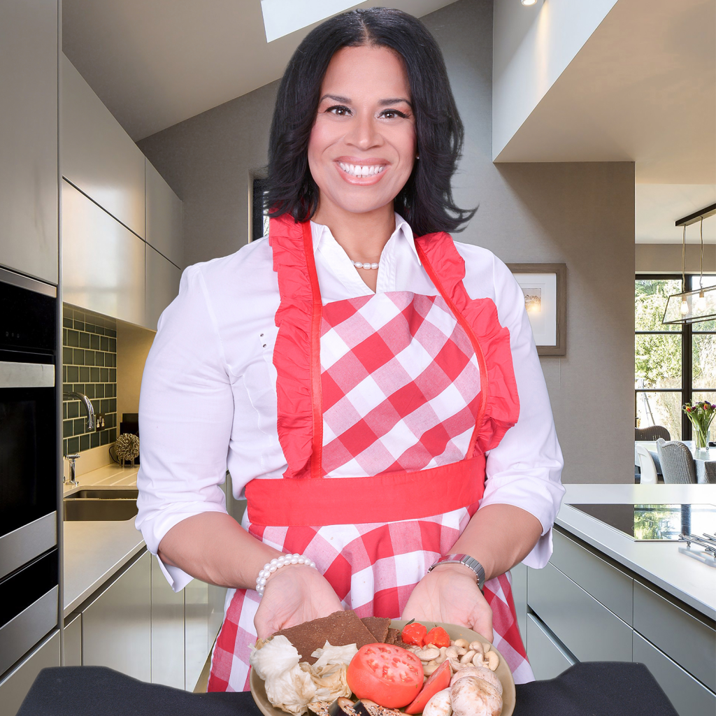 A female chef in a red plaid apron presenting a dish