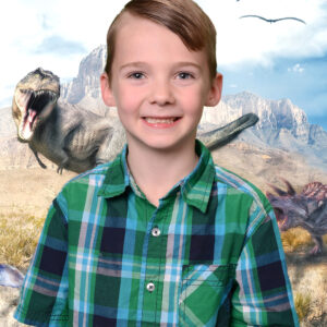 A school portrait of a young boy in front of a dinosaur background